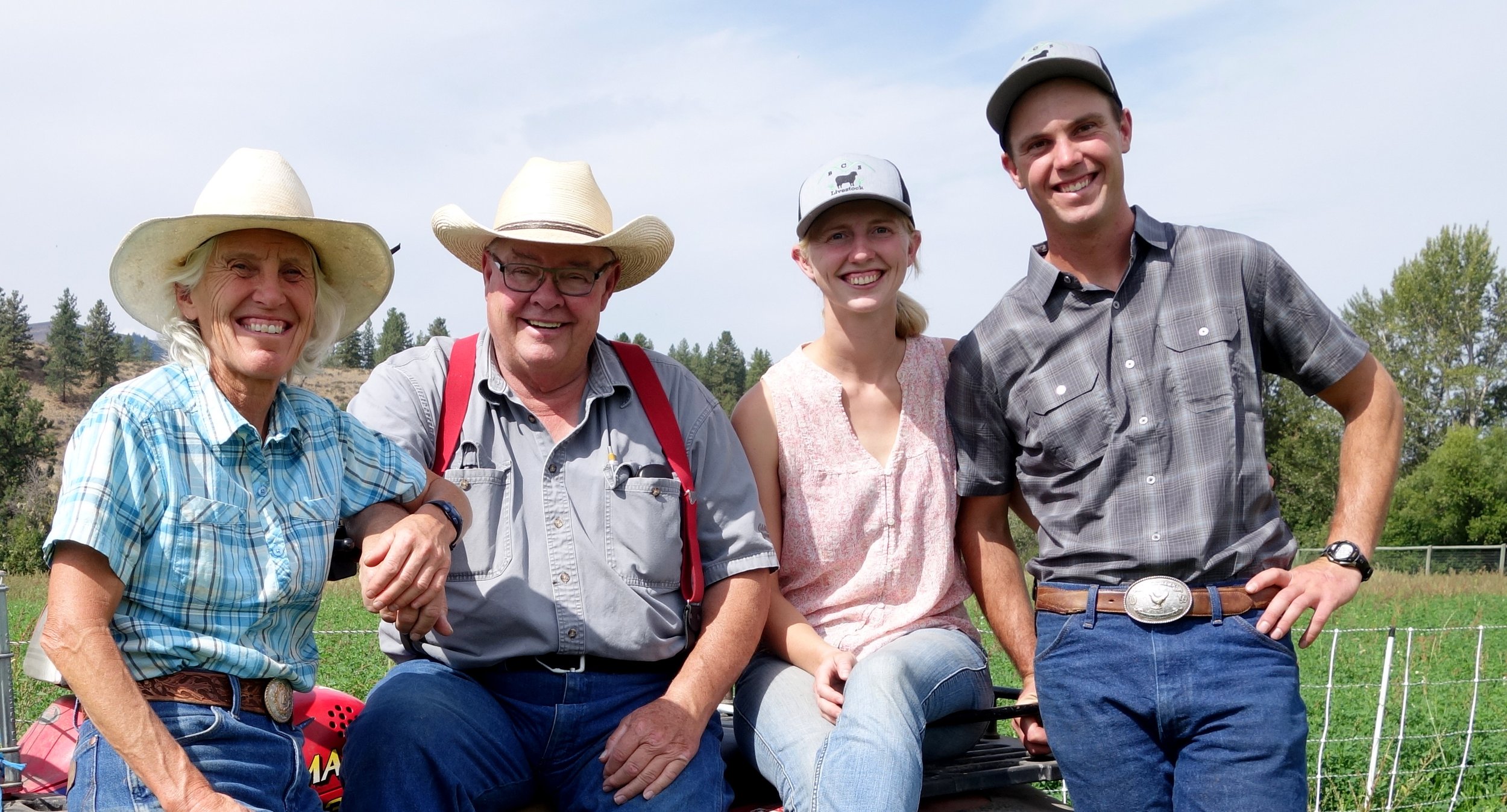 Four farmers smiling together outdoors, wearing hats and casual clothing, with a scenic rural landscape in the background, showcasing a sense of community and agriculture.