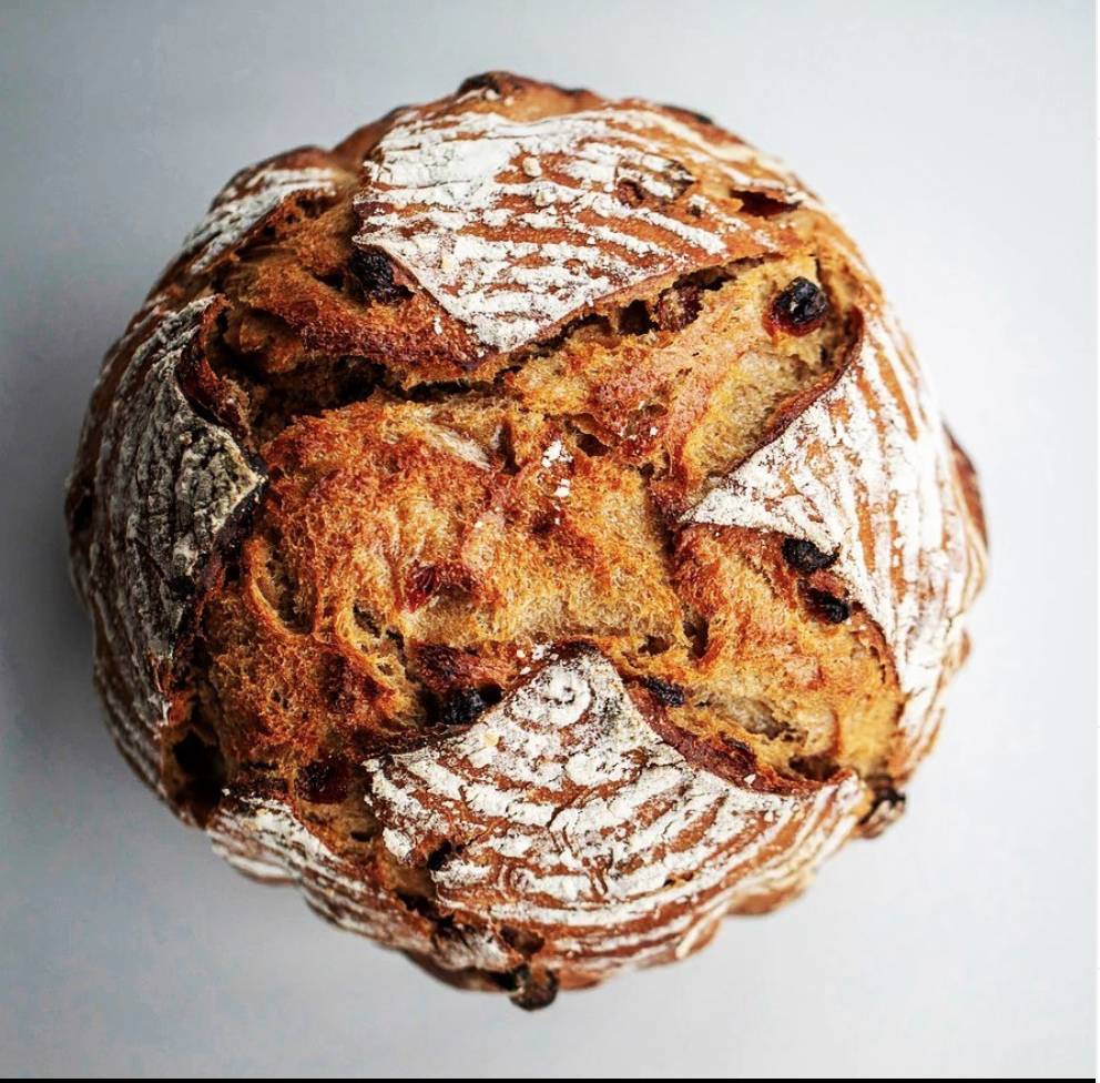 Artisan round sourdough bread with a crusty exterior and decorative scoring on top, showcasing a golden-brown color and a rustic appearance.